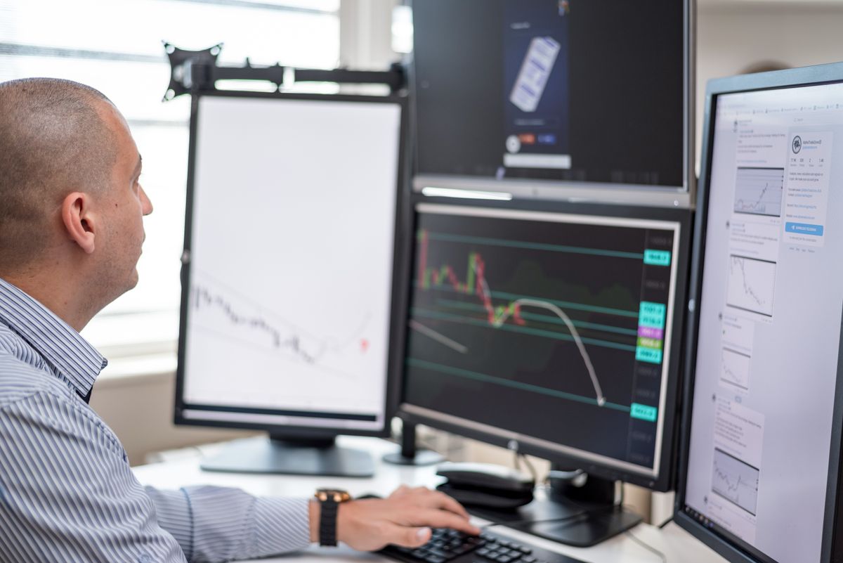 A trader's workstation with several monitors displaying financial charts and market data, illustrating the data environment in which AI currency-exposure models operate.
